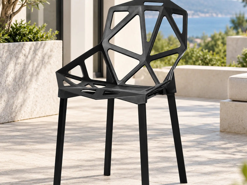 Black outdoor armchair with geometric cutouts in the back and seat on a sunny patio.