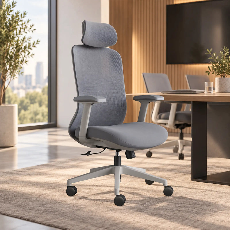 A modern gray fabric office chair with a headrest, adjustable armrests, and a five-wheel base, positioned in a bright, contemporary office space with a desk and other chairs in the background.