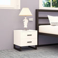 White Bedside Buddy two-drawer cabinet with dark legs beside a bed